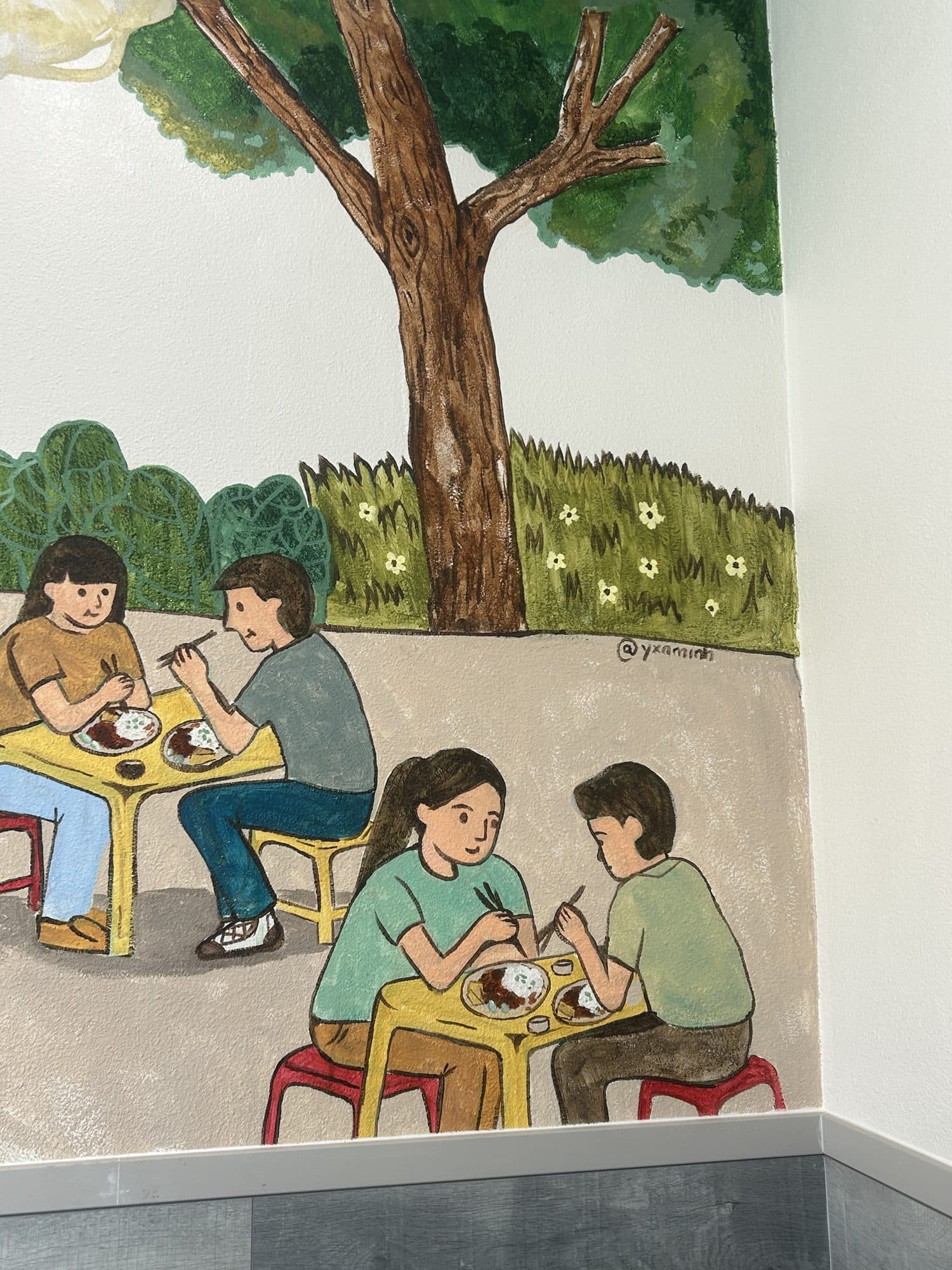 Painted diners eating at small tables on red stools under a tree