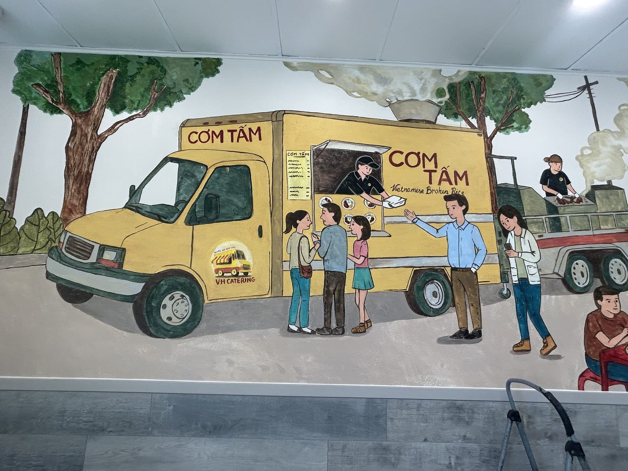 Close view of the cơm tấm food truck mural with people ordering at the window