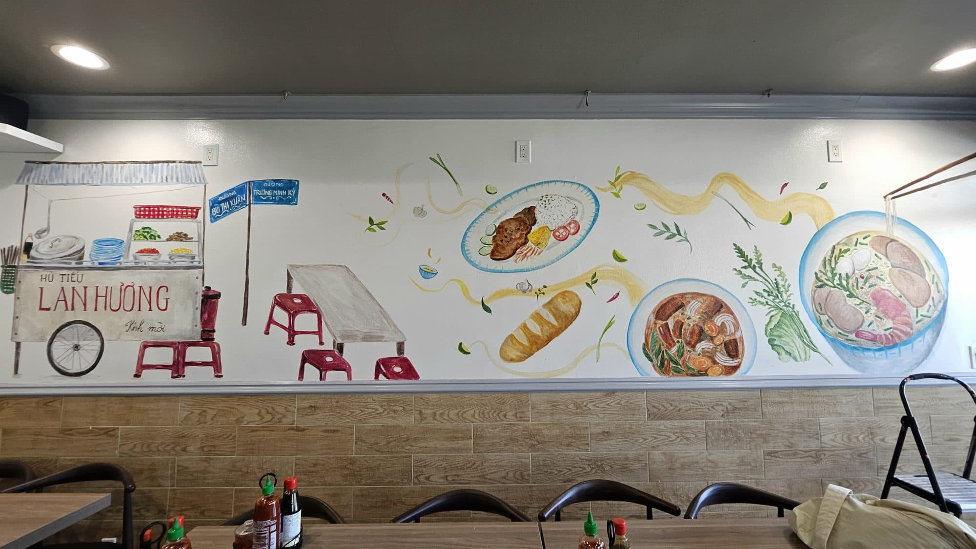 Mural of phở bowls, bánh mì and a street food cart along a Vietnamese restaurant dining room wall