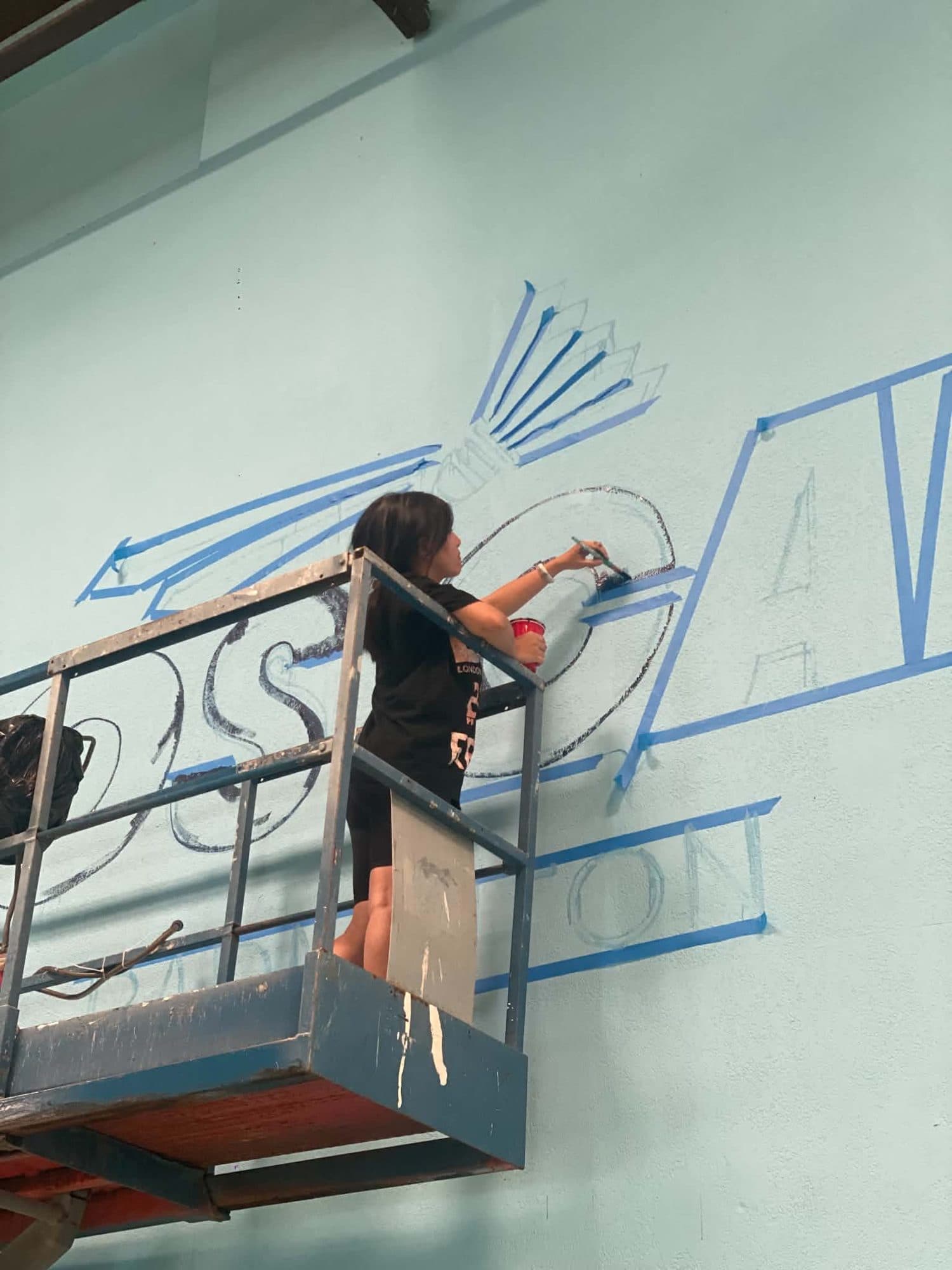 Muralist outlining the LOS CAB logo with tape on a lift