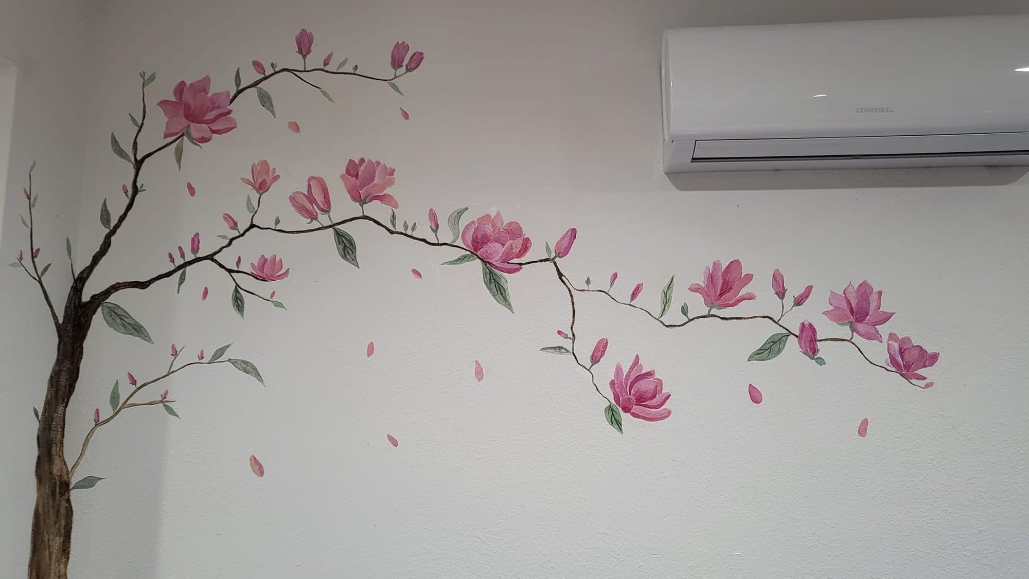 Pink magnolia branch mural painted across a bedroom accent wall