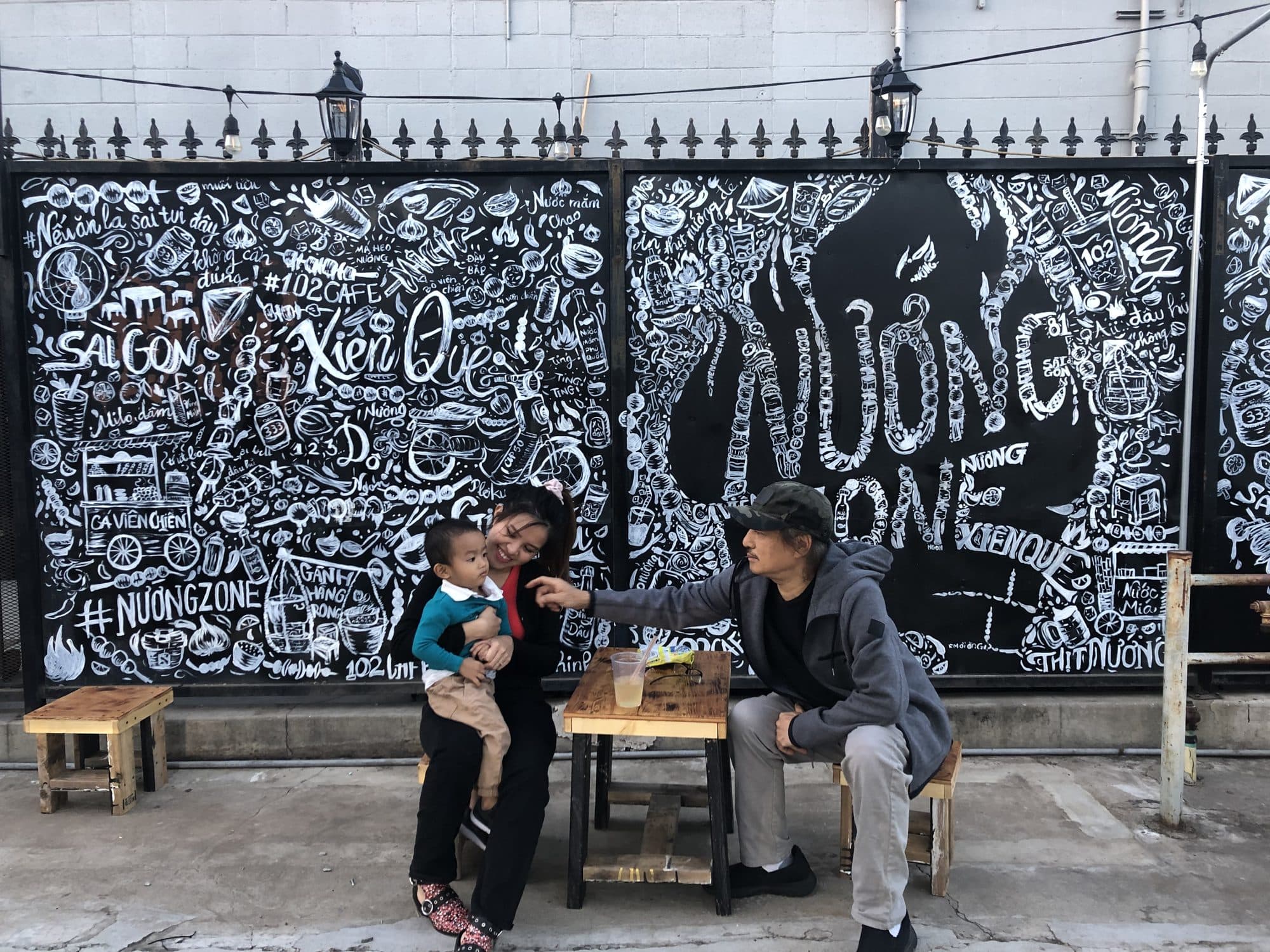 Family dining in front of the Nướng Zone hand-lettered patio wall